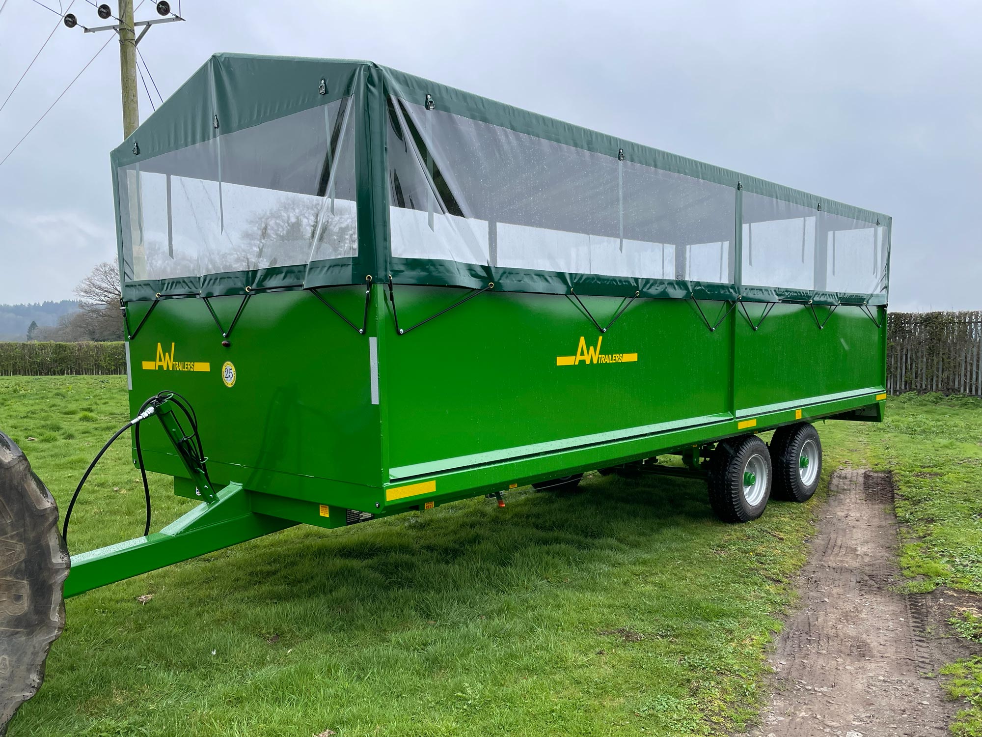 A large green trailer with a waterproof cover in a green grass field