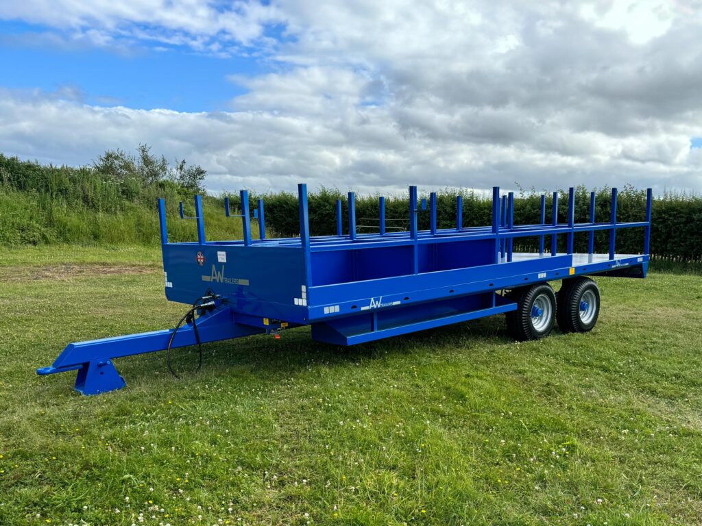 A Large blue trailer with scaffold poles in a green grass field