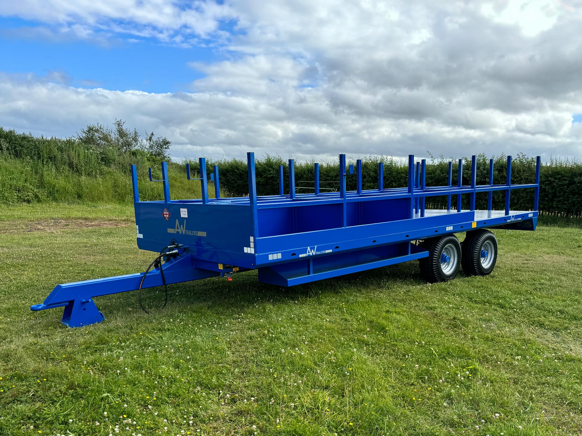 A Large blue trailer with scaffold poles in a green grass field