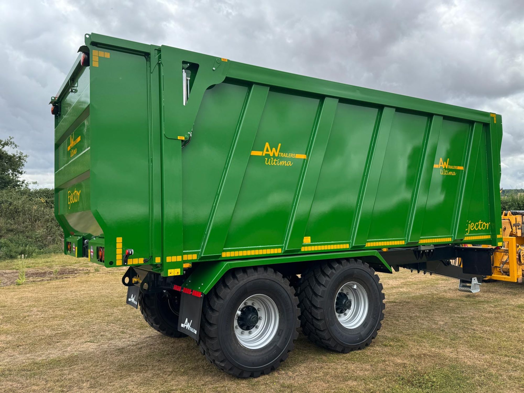 A large green trailer with large black tyres in a field
