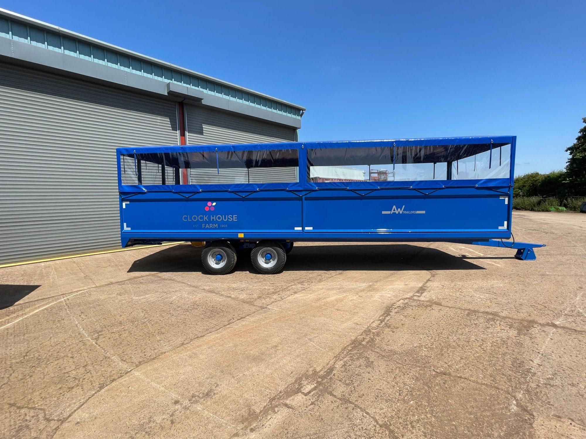A Large blue people carrier trailer with cover on top in a factory carpark