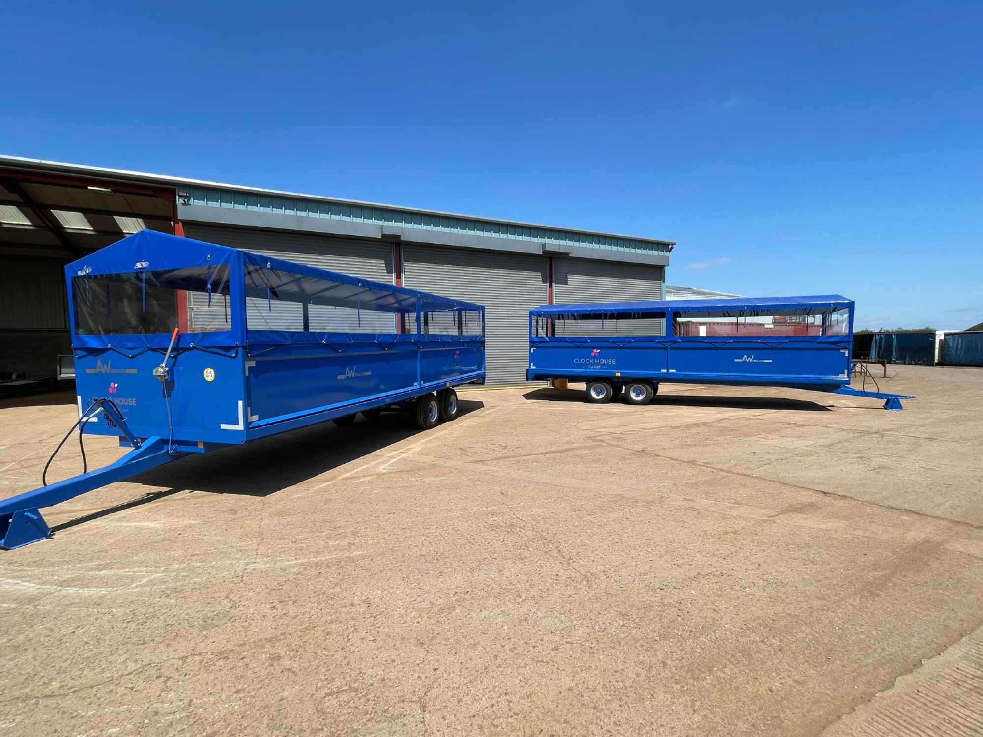 2 Large blue people carrier trailers with cover on top in a factory car park