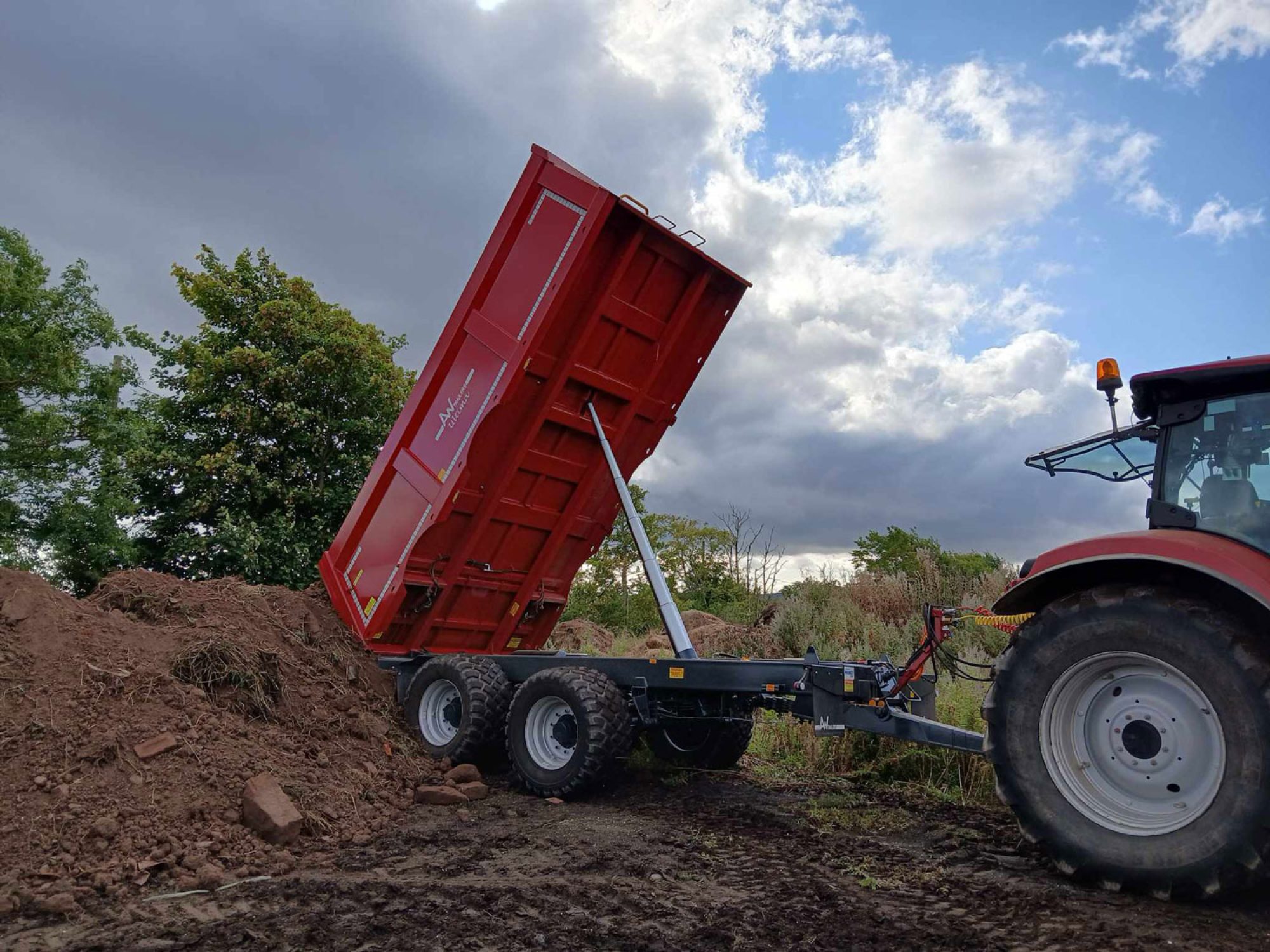 Red Stone & Rubble Trailer in a field tipping dirt into a pile
