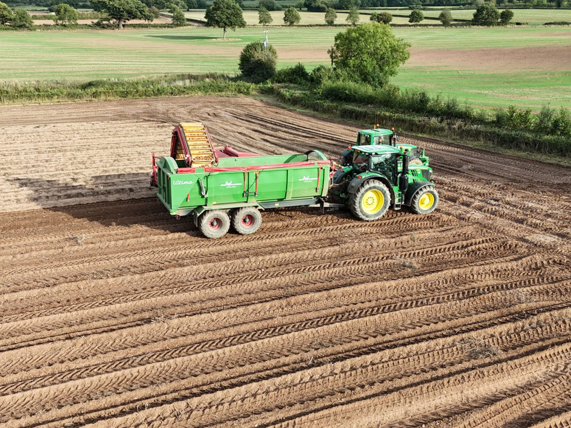 A large Ultima Potato & Root trailer working in a field being pulled by a tractor